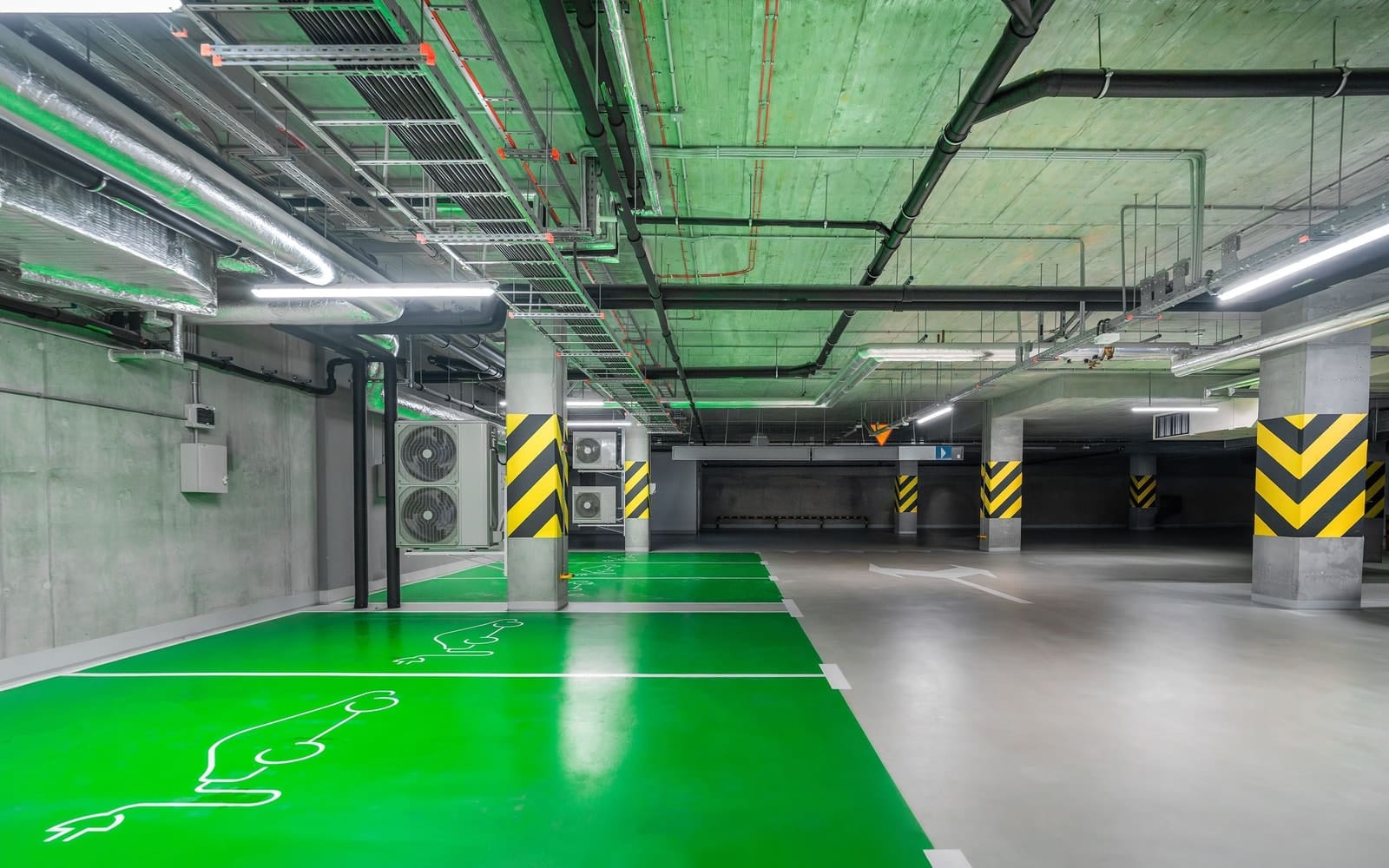 Kapalı bir otoparkta yeşile boyanmış, elektrikli araç şarj simgesiyle işaretlenmiş park yerleri