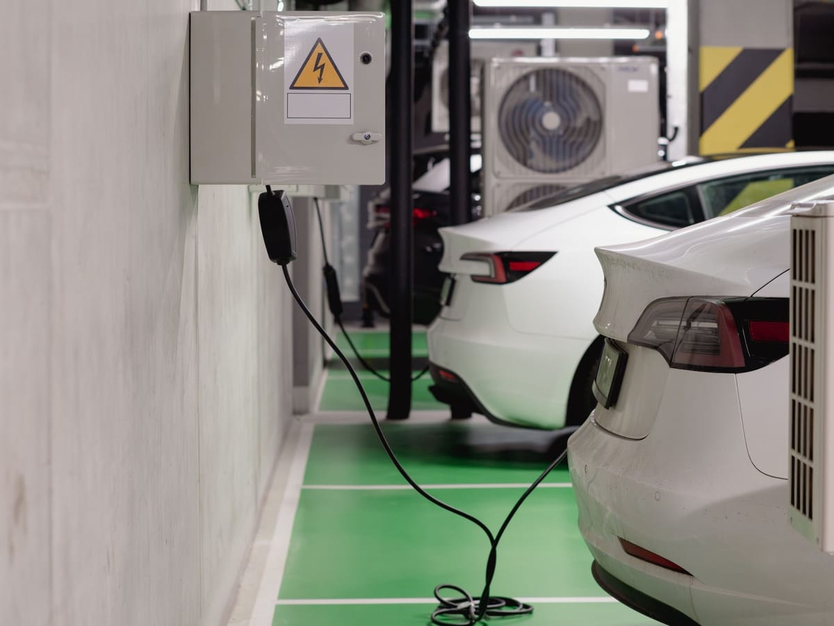 Kapalı otoparkta duvardaki elektrik panosuna bağlı kabloyla şarj edilen beyaz elektrikli otomobiller