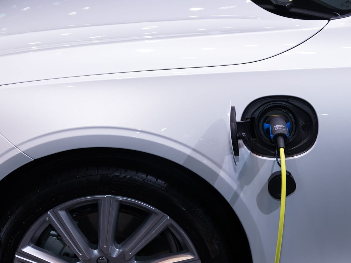Beyaz bir elektrikli otomobilin şarj soketine takılı, sarı kablolu şarj fişi