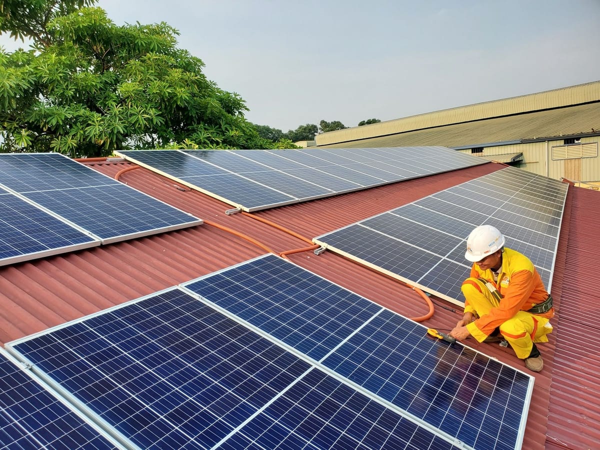 Kırmızı trapez sac çatıda güneş panellerini kontrol eden teknisyen